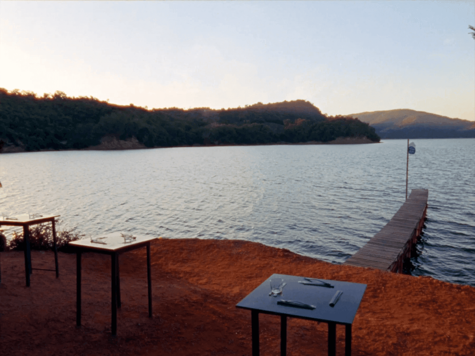 Un pontile di legno su un lago al tramonto, con tavolini apparecchiati e il sole radente sull'acqua.